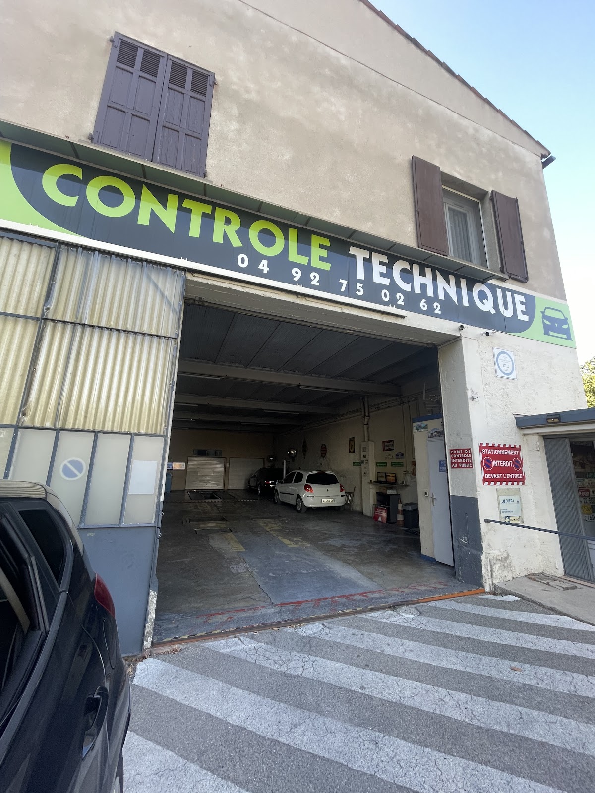 Entrée du centre de contrôle technique de Mane : enseigne verte et anthracite avec le numéro de téléphone, piste de contrôle visible à l'intérieur